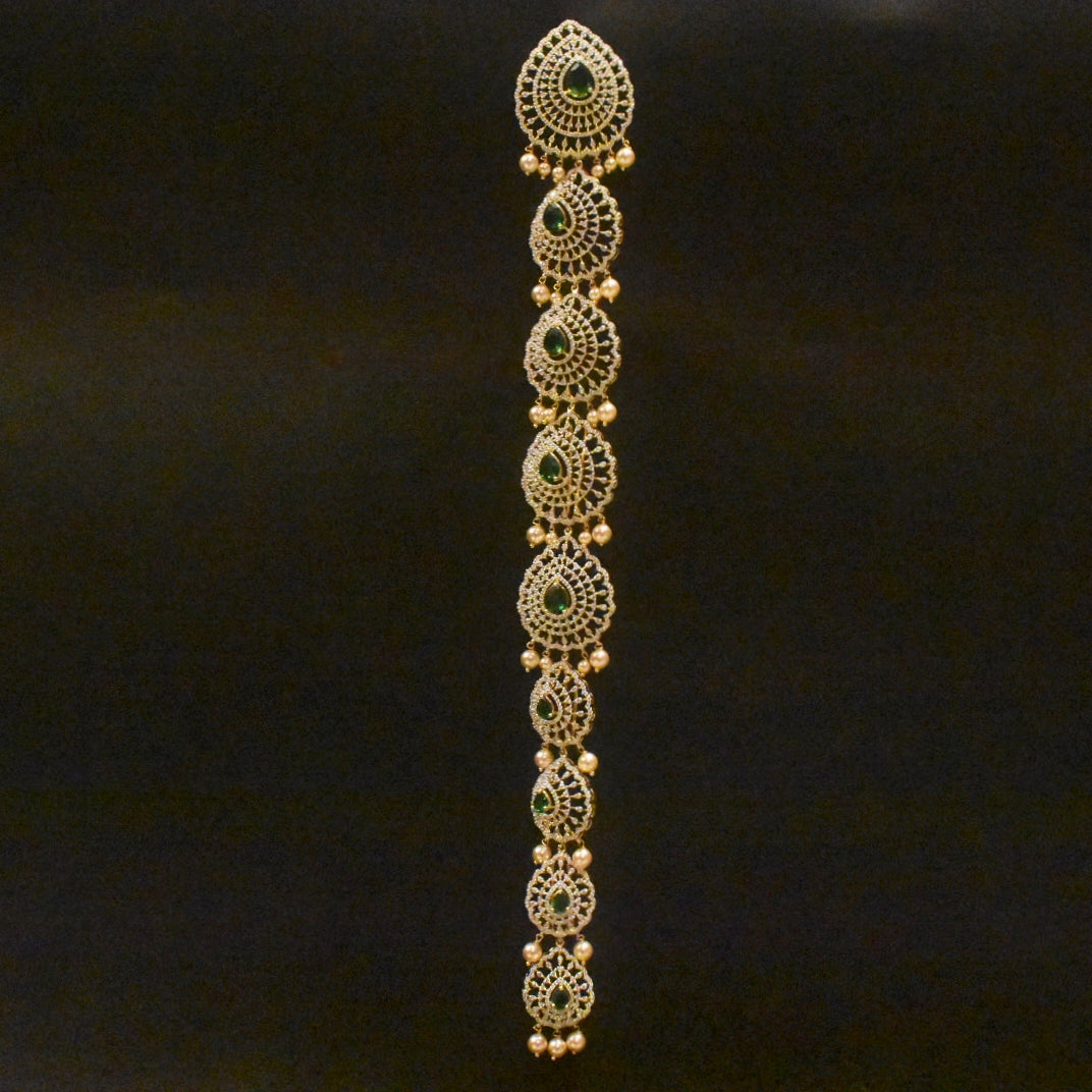 Decorative gold bracelet with green stones on a black background