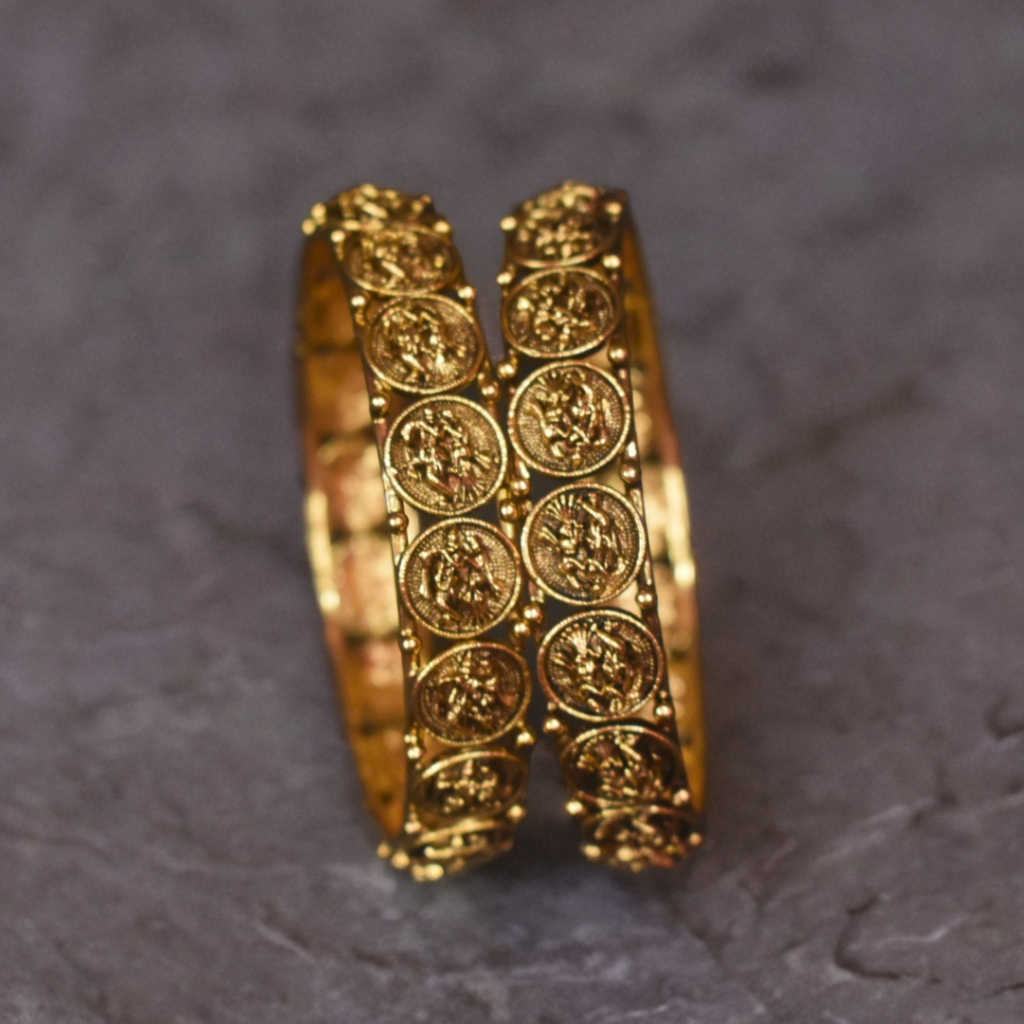 Pair of gold bangles with intricate designs on a dark gray background