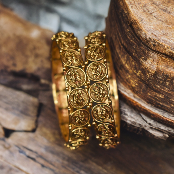 Gold bangles with intricate designs on a wooden surface