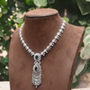 Elegant silver necklace with green gemstones on a brown velvet stand against a natural background