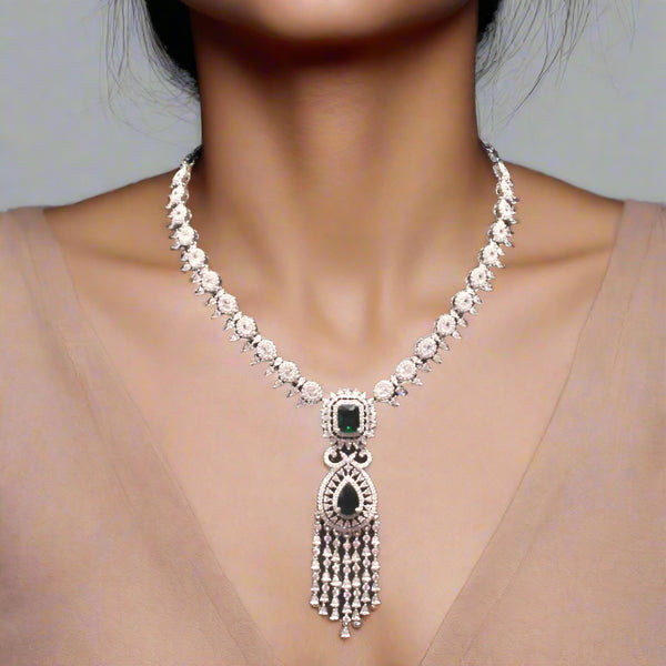 Silver necklace with green gemstone on a brown velvet stand, with bangles in the background