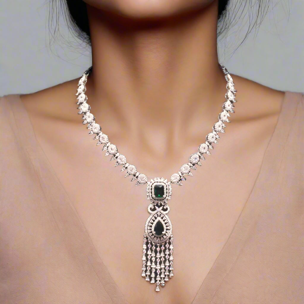 Silver necklace with green gemstone on a brown velvet stand, with bangles in the background
