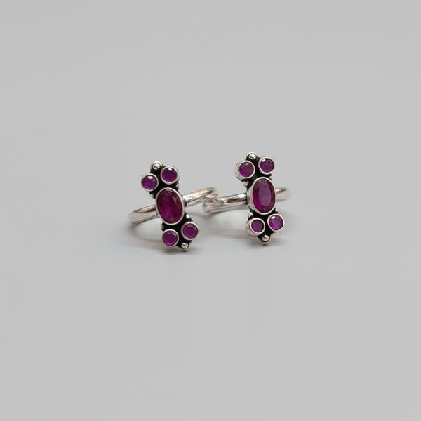 A pair of 92.5 silver ruby and emerald adorned bichiya toe rings placed on a red leaf background.