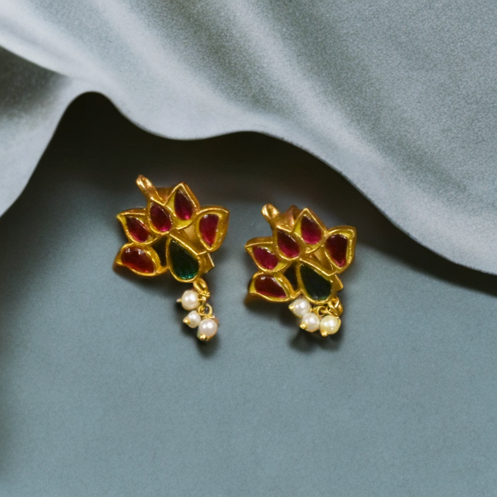 Pair of gold earrings with red and green gemstones and pearl drops on a gray background