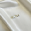 Real pearl stud earrings flat lay on ivory silk