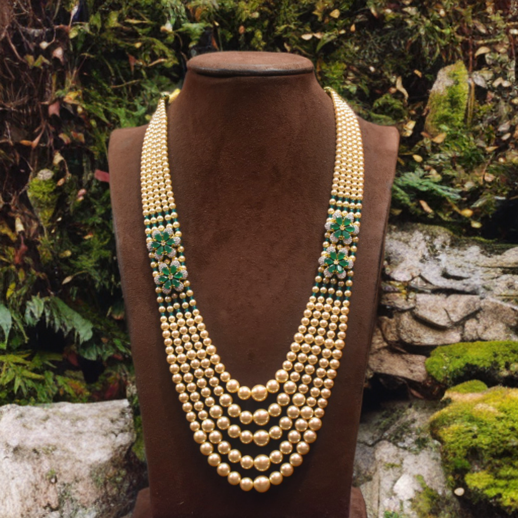 Multi-layered pearl necklace with green accents on a brown mannequin against a natural stone and foliage background.