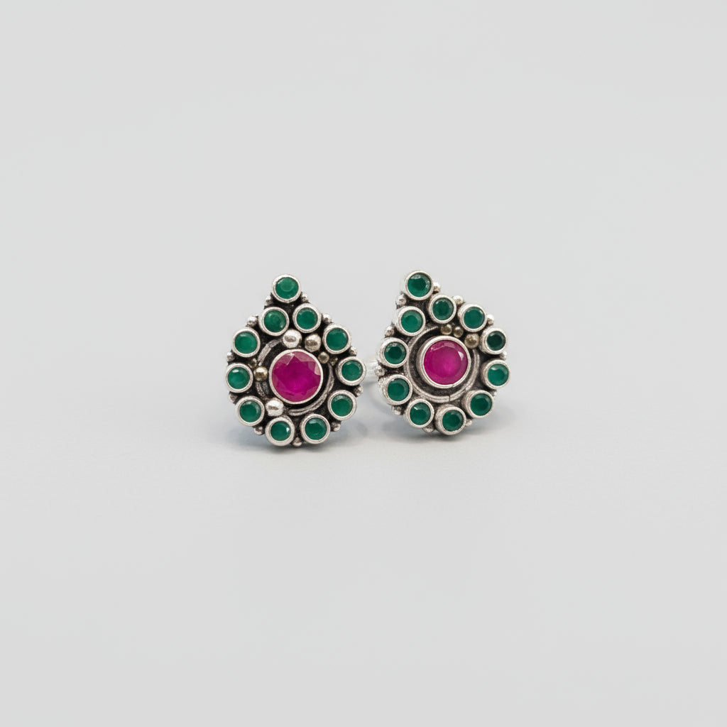 A pair of silver toe rings with red and green stone accents placed on a green leaf.