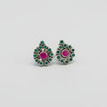 A pair of silver toe rings with red and green stone accents placed on a green leaf.