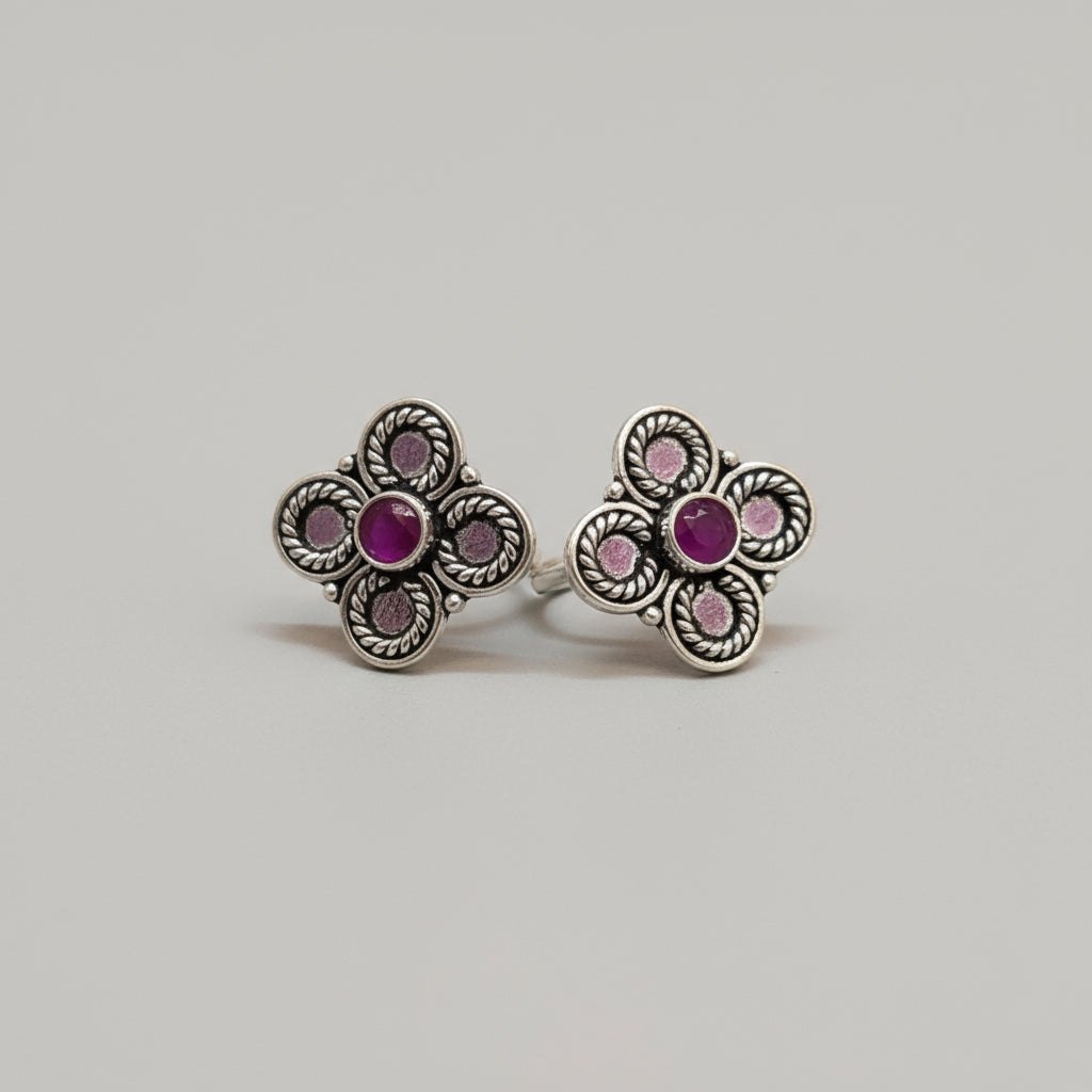 A pair of 92.5 silver toe rings with ruby and emerald embellishments, placed on a red leaf background.