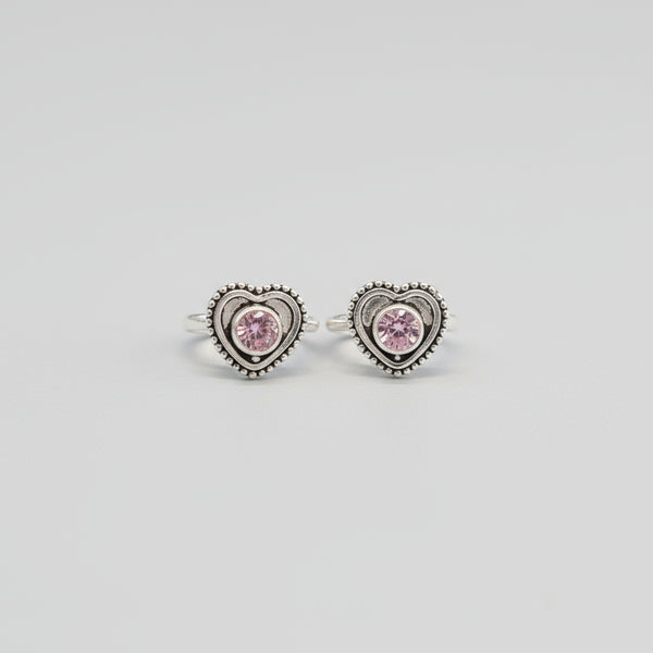 A pair of silver toe rings with heart-shaped cubic zirconia embellishments, placed on a red leaf background.