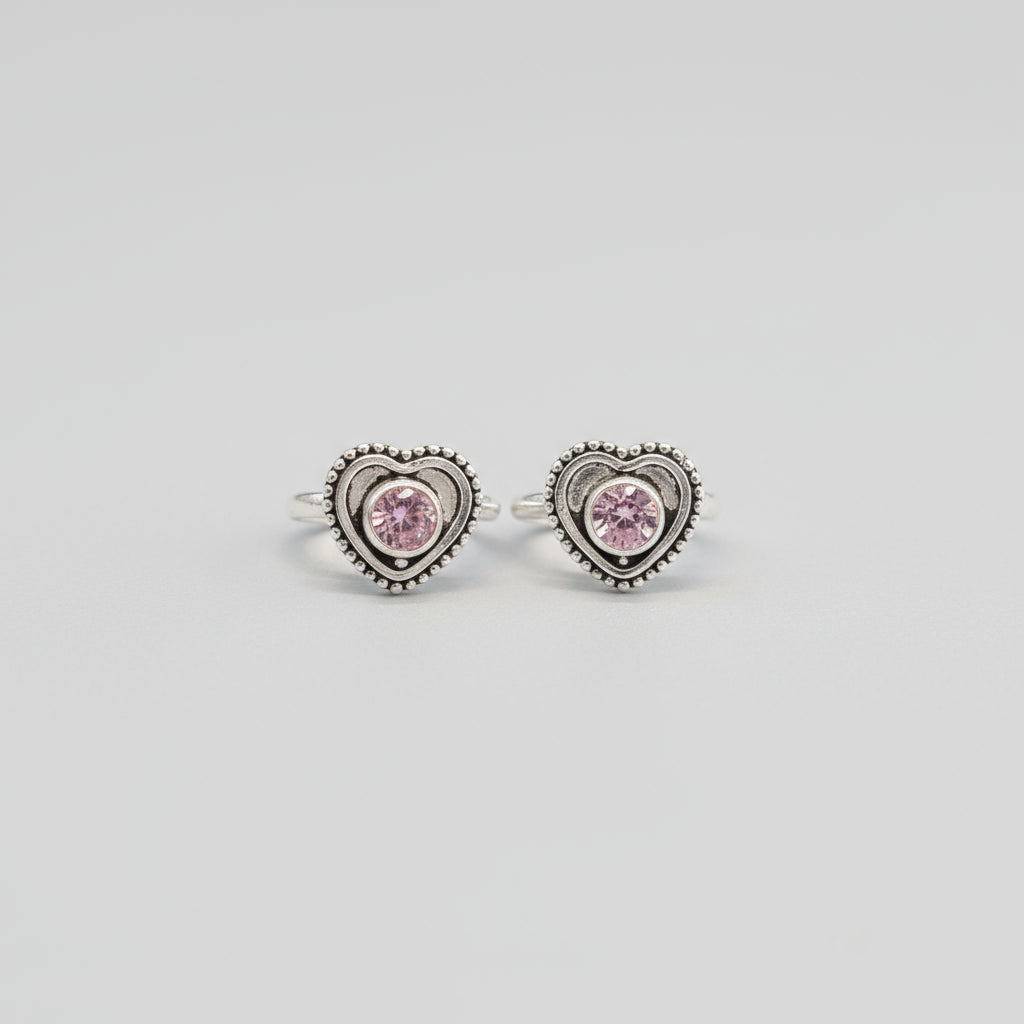 A pair of silver toe rings with heart-shaped cubic zirconia embellishments, placed on a red leaf background.
