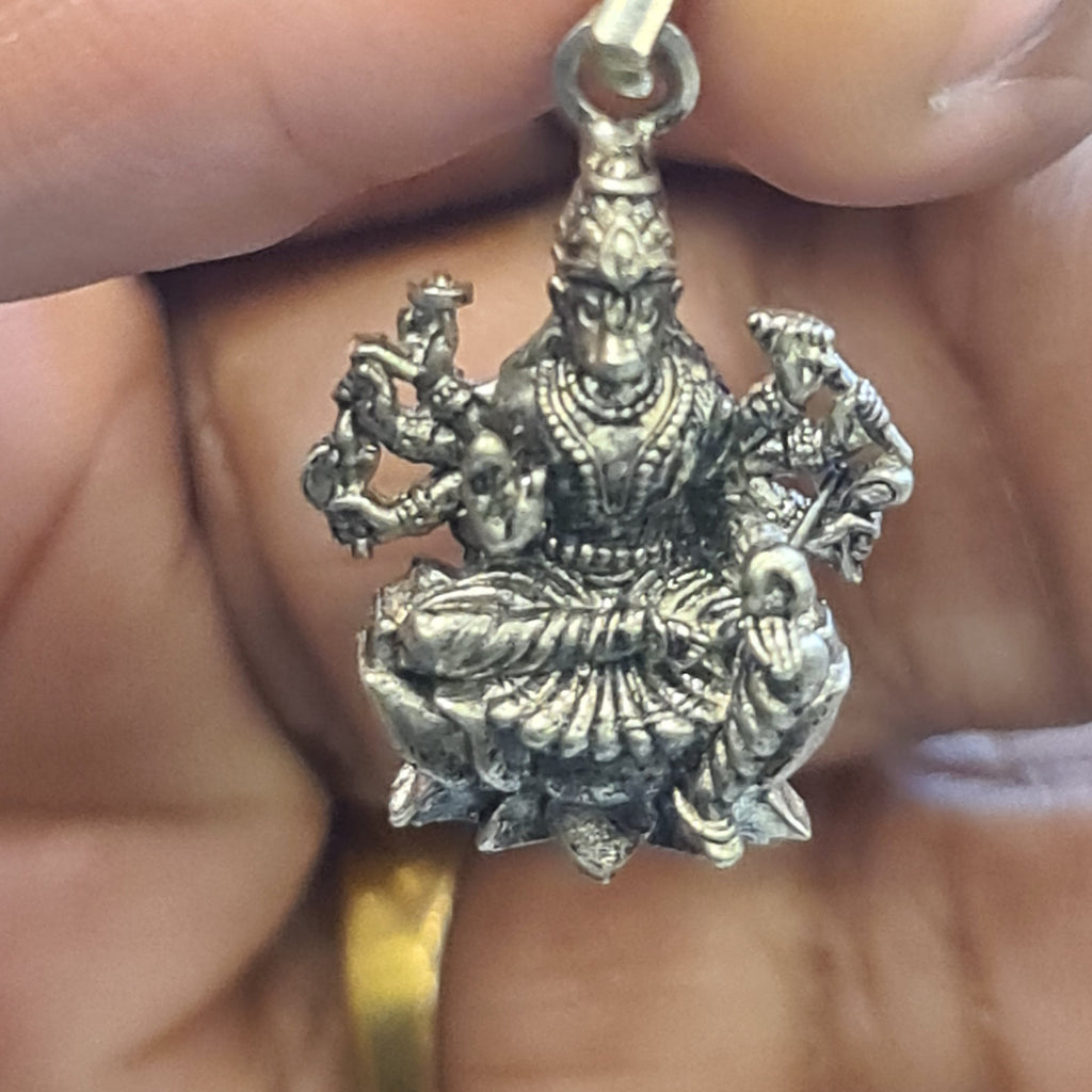 Silver dragon pendant held between fingers with a blurred background